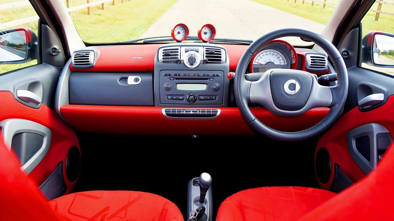 Detailed view of a red Smart Fortwo car's dashboard and steering wheel interior.